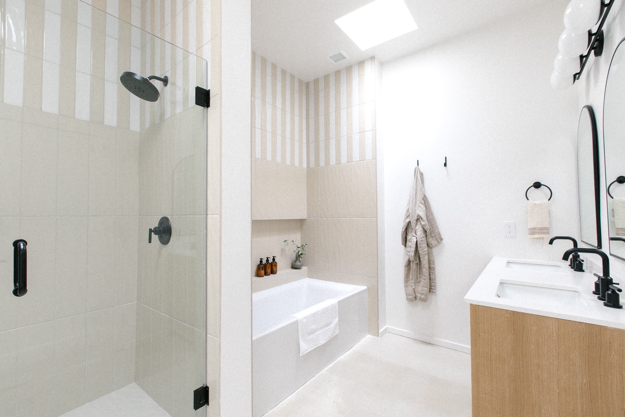 A bright, modern bathroom featuring a glass-enclosed walk-in shower, a soaking tub, and a double vanity with round mirrors and black fixtures.