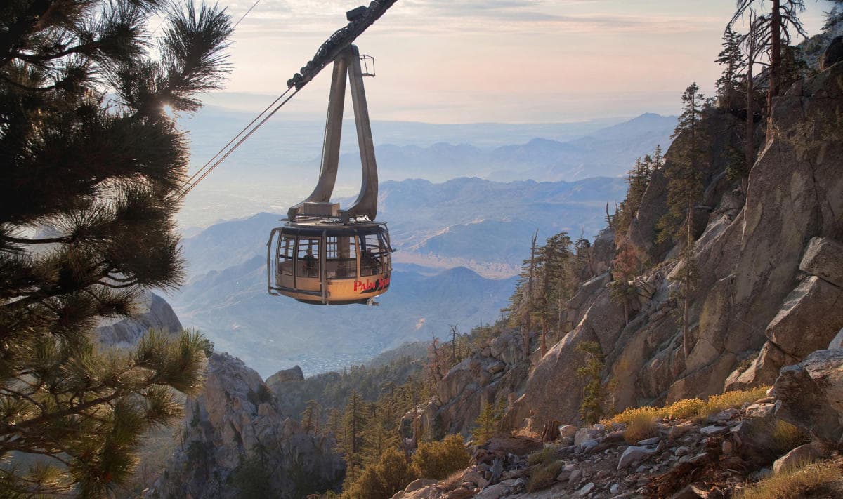 A gondola lifts over a mountainous landscape during sunset.