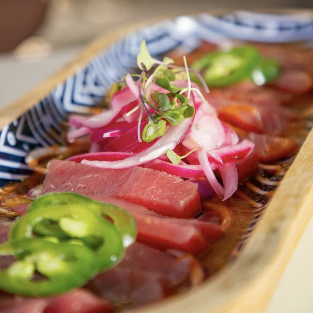 A platter of sliced tuna topped with pickled onions, microgreens, and jalapeño slices.