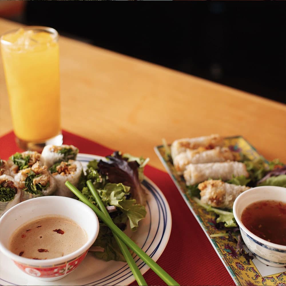 A plate of fresh spring rolls, lettuce, dipping sauce, and a glass of orange drink.