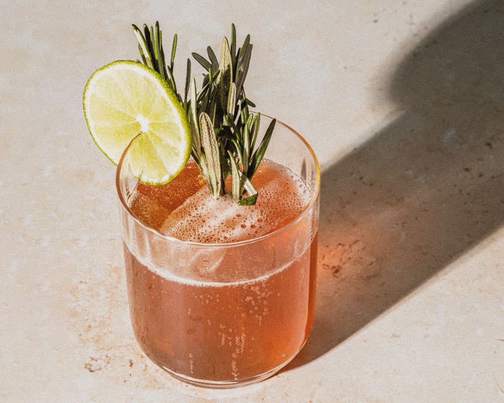 A refreshing cocktail garnished with a lime slice and rosemary sprigs.